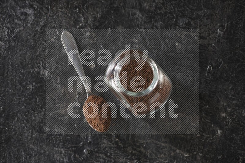 وعاء زجاجي للبهارات وملعقة معدنية ممتلئان ببودرة القرنفل على أرضية سوداء