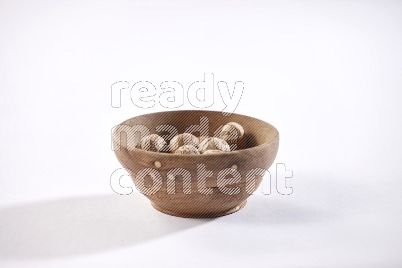 A wooden bowl full of nutmeg on a white flooring in different angles