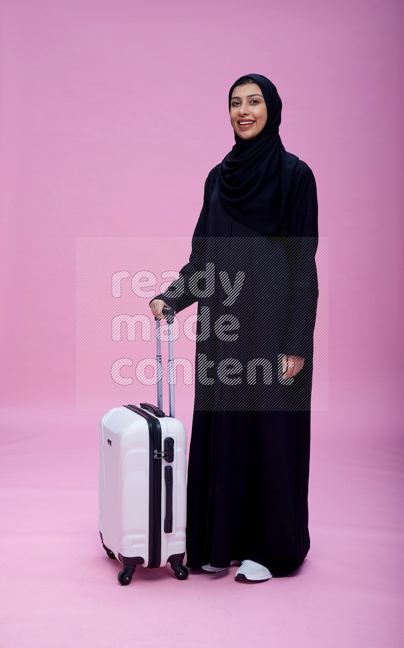 Saudi woman wearing Abaya standing holding bag on pink background