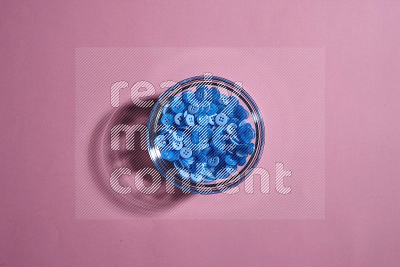 A glass bowl full of colored buttons on rose background