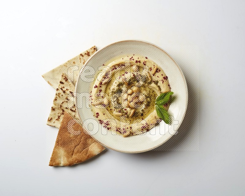 Hummus in a pottry plate garnished with zaatr & sumak on a white background