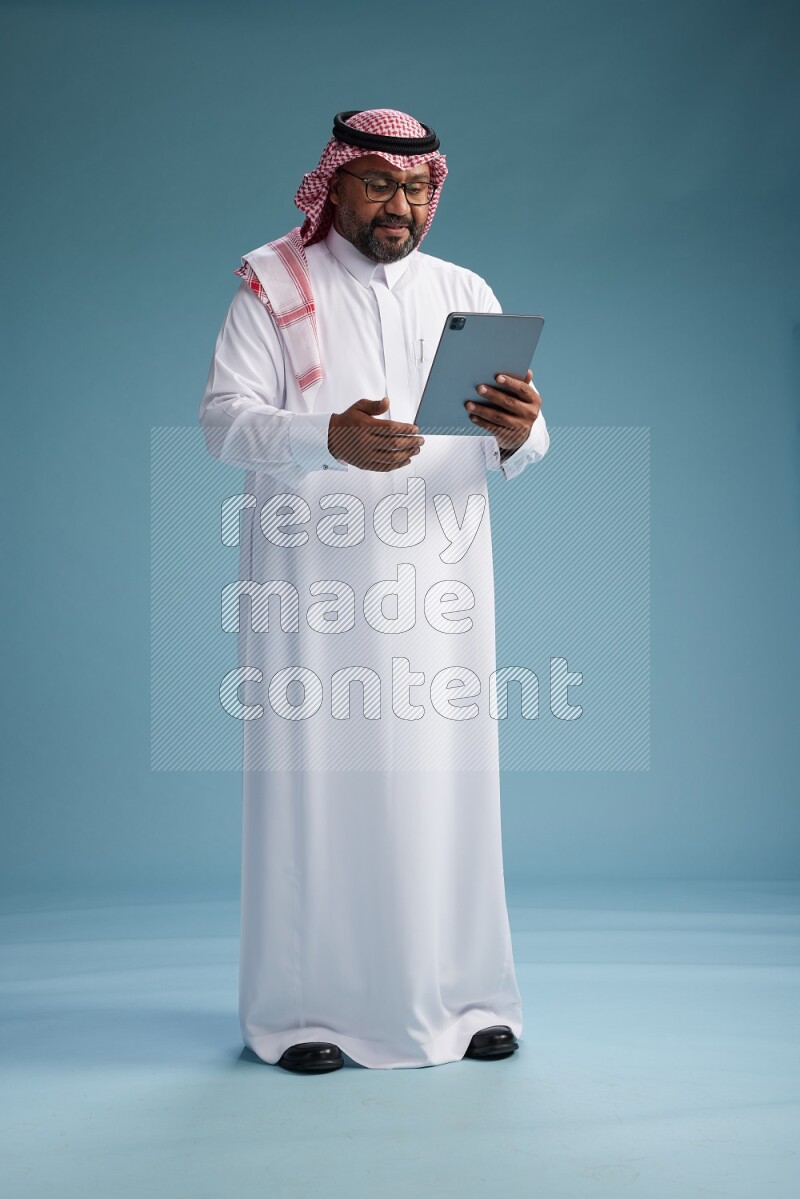 Saudi Man with shimag Standing holding a tablet on blue background