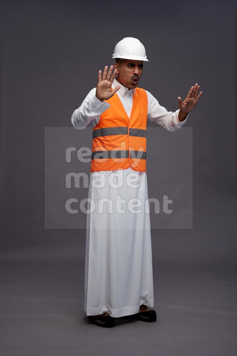 Saudi man wearing thob with engineer vest standing interacting with the camera on gray background