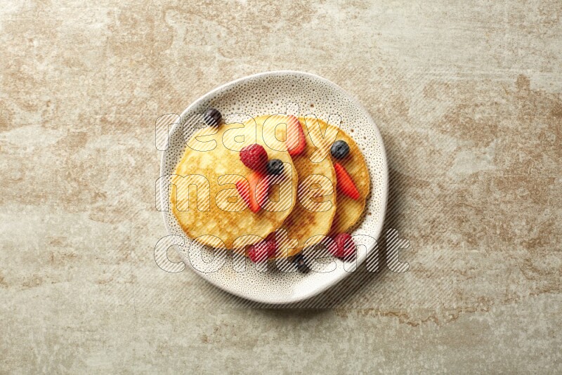 Three stacked mixed berries pancakes in an irregular plate on beige background