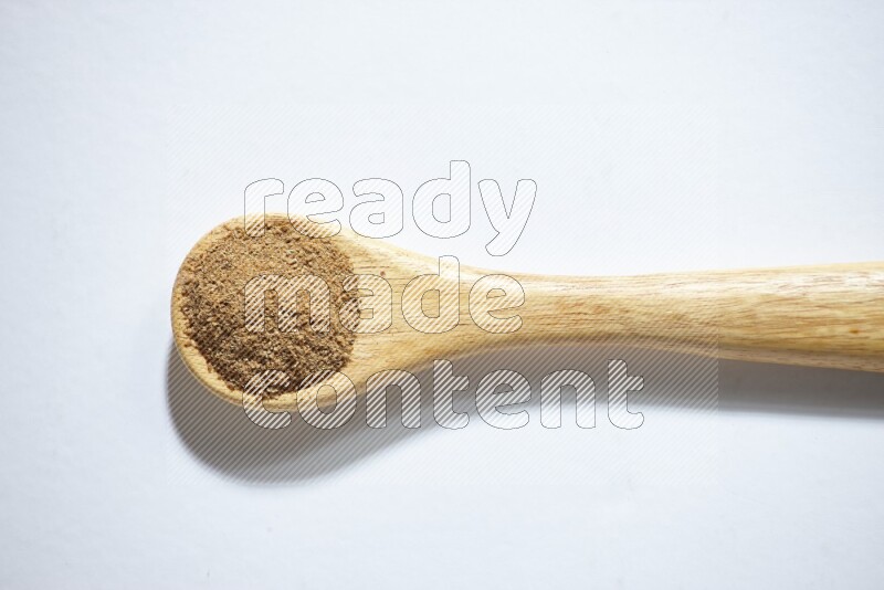 A wooden spoon full of cumin powder on a white flooring