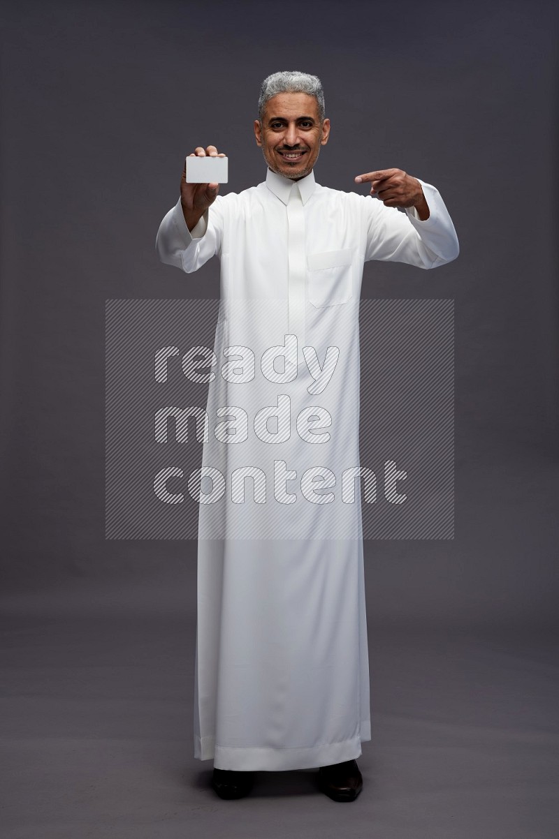 Saudi man wearing thob standing holding ATM card on gray background