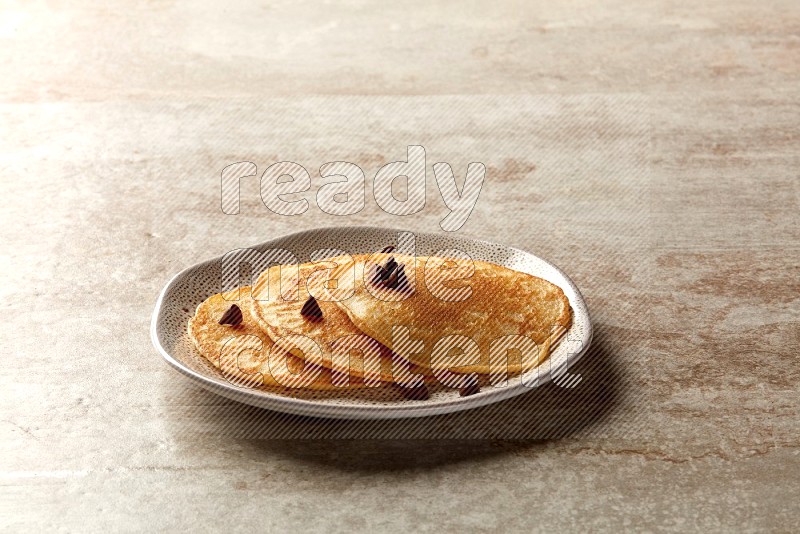 Three stacked chocolate chips pancakes in an irregular plate on beige background