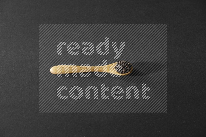 حبوب الفلفل الأسود في ملعقة خشبية علي خلفية سوداء