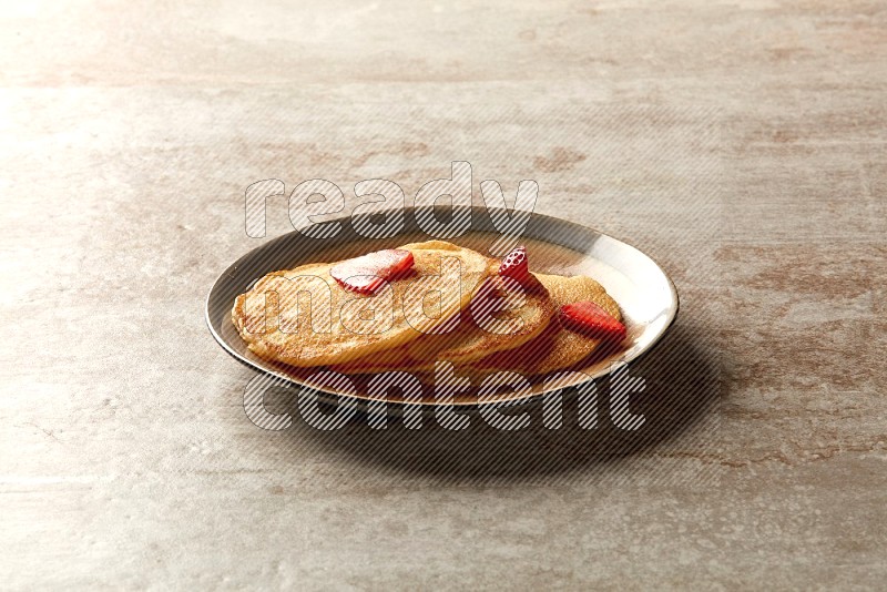 Three stacked strawberry pancakes in a bicolor plate on beige background