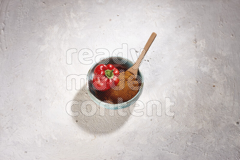 A colored pottery plate full of ground paprika powder and red bell pepper on white background