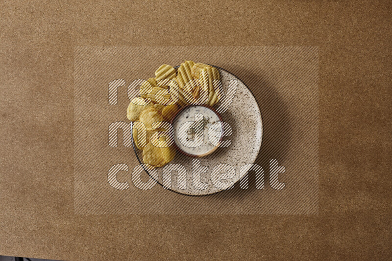 Assorted snacks on a pottery plate with a dipping on brown background