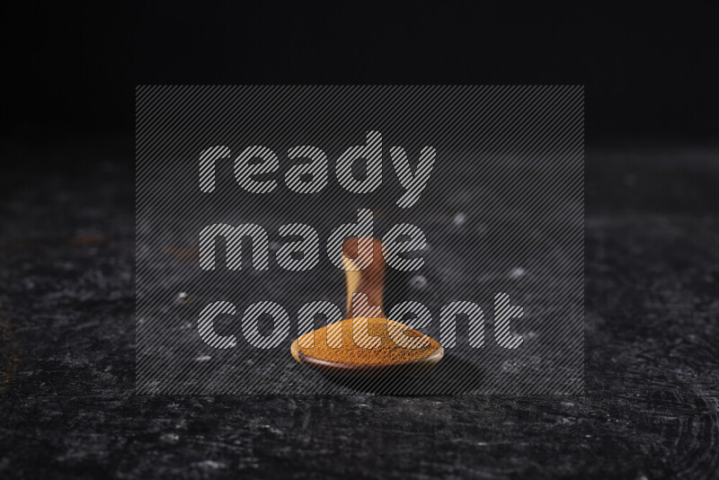 A wooden ladle full of ground paprika powder on black background