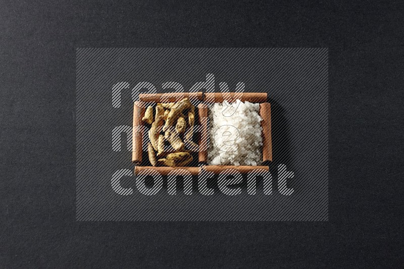 2 squares of cinnamon sticks full of white salt and turmeric fingers on black flooring