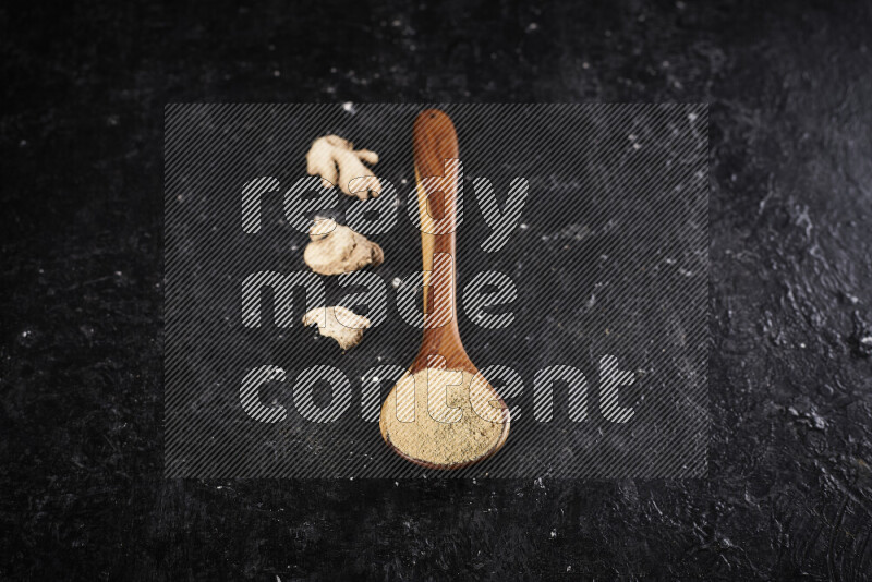 A wooden ladle full of ground ginger powder on black background