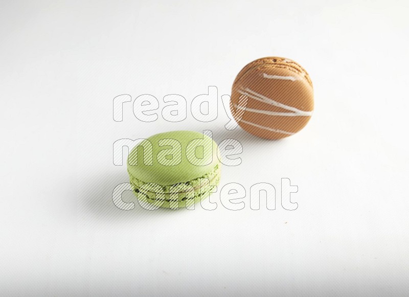 45º Shot of of two assorted Brown Irish Cream, and Green Pistachio macarons on white background