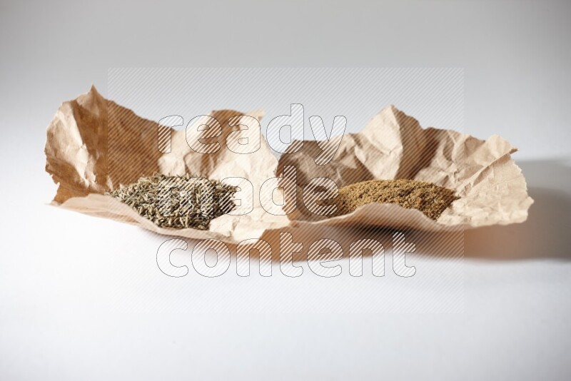 Cumin seeds and cumin powder in 2 crumpled pieces of paper on white flooring