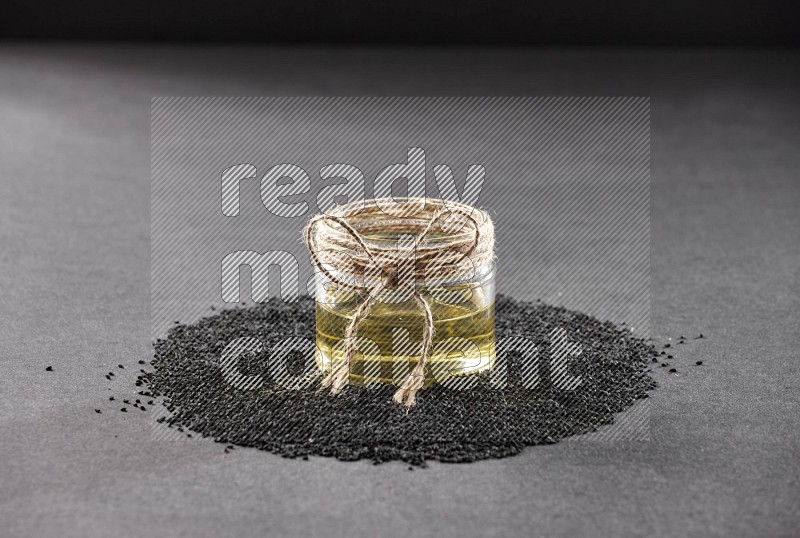 A glass jar full of black seeds oil surrounded by the seeds on a black flooring in different angles