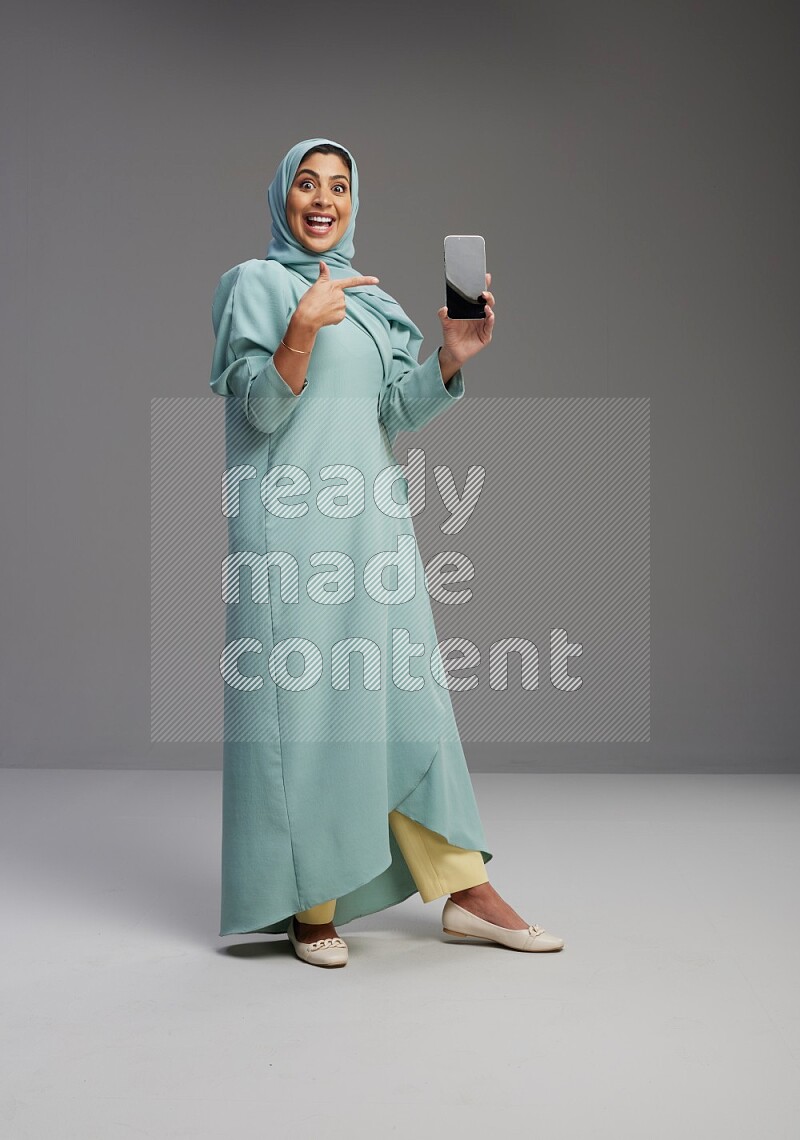 Saudi Woman wearing Abaya standing showing phone to camera on Gray background