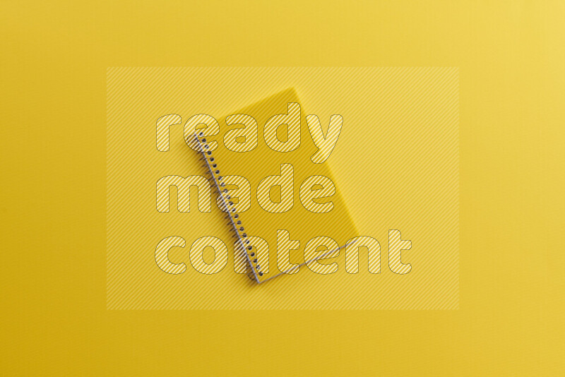 A yellow notebook with different school supplies on yellow background