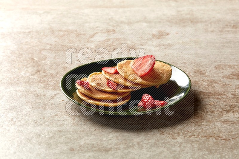 Five stacked strawberry mini pancakes in a green plate on beige background