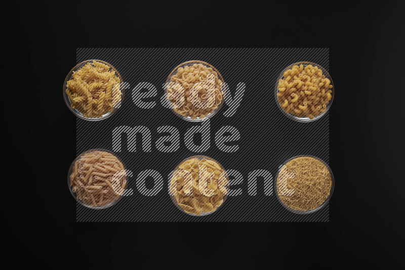 Different pasta types in 6 glass bowls on black background