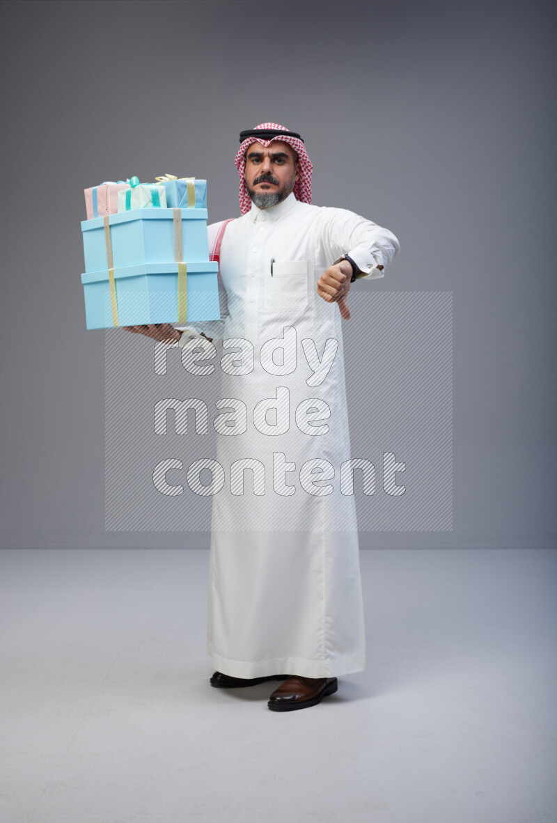 Saudi man Wearing Thob and red Shomag standing holding gift box on Gray background