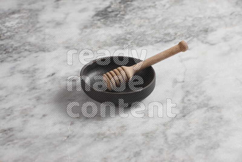 Black pottery bowl with wooden honey dipper in it on grey marble background