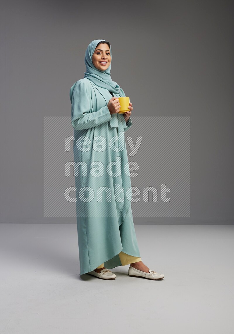 Saudi Woman wearing Abaya standing  holding a mug on Gray background