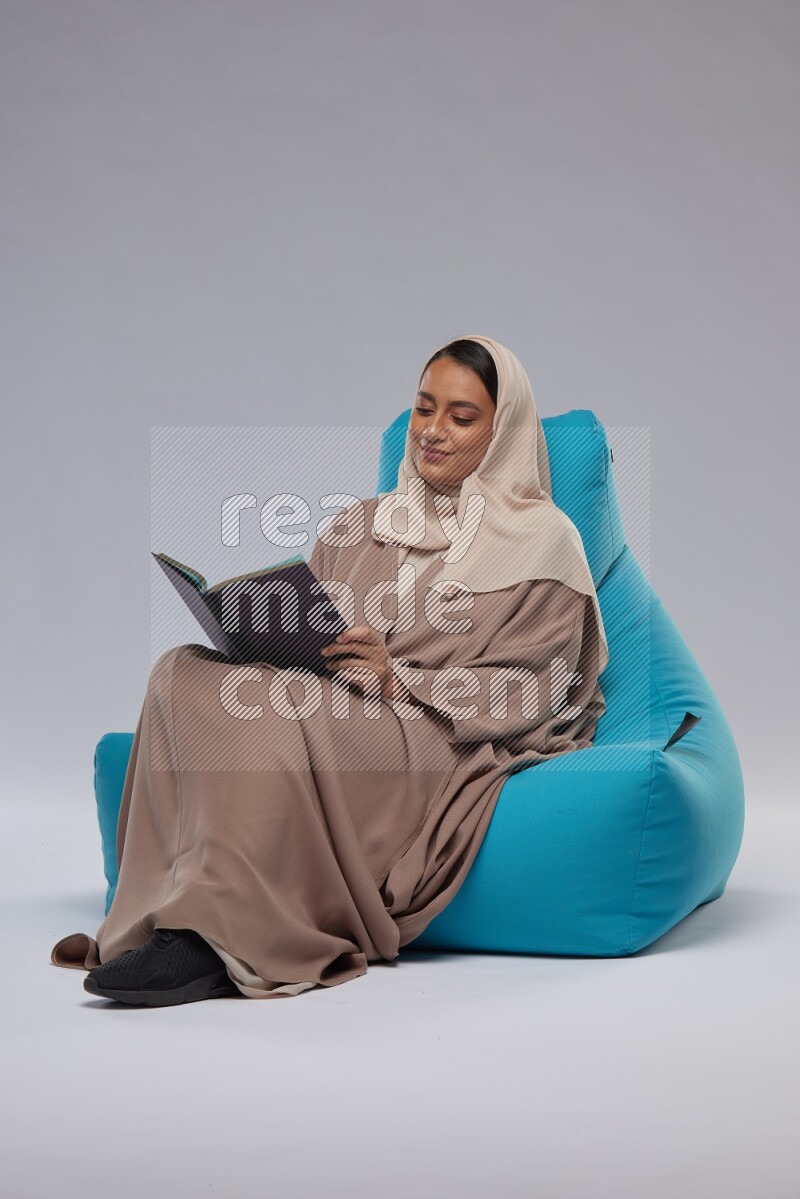 A woman sitting on a blue beanbag and reading a book