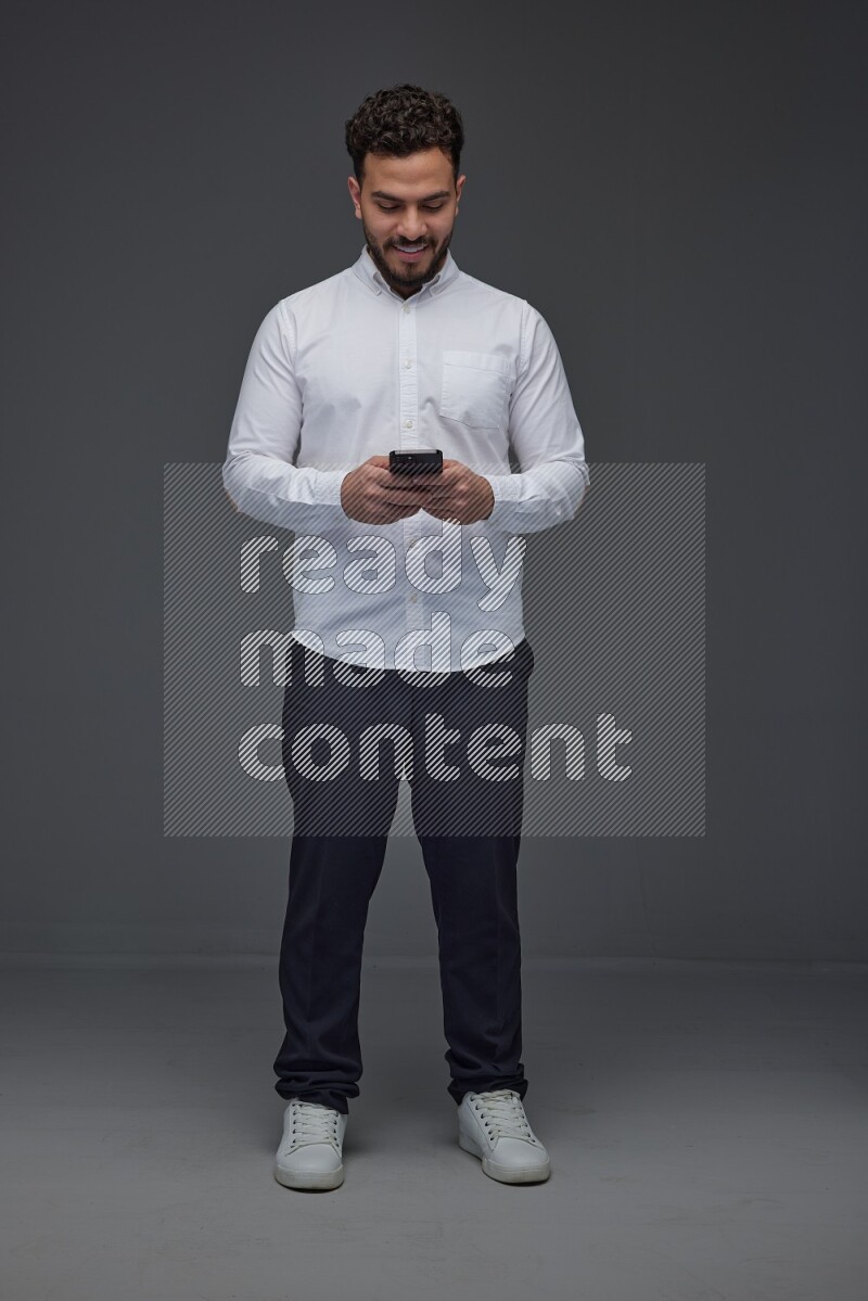 A man wearing smart casual standing and using his phone eye level on a gray background