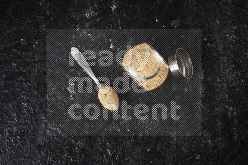 A glass jar full of ground ginger powder on black background