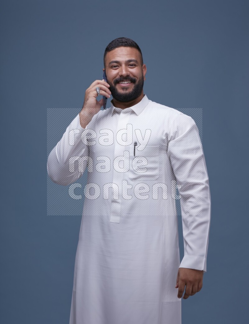A Saudi man calling on blue background wearing Saudi Thob