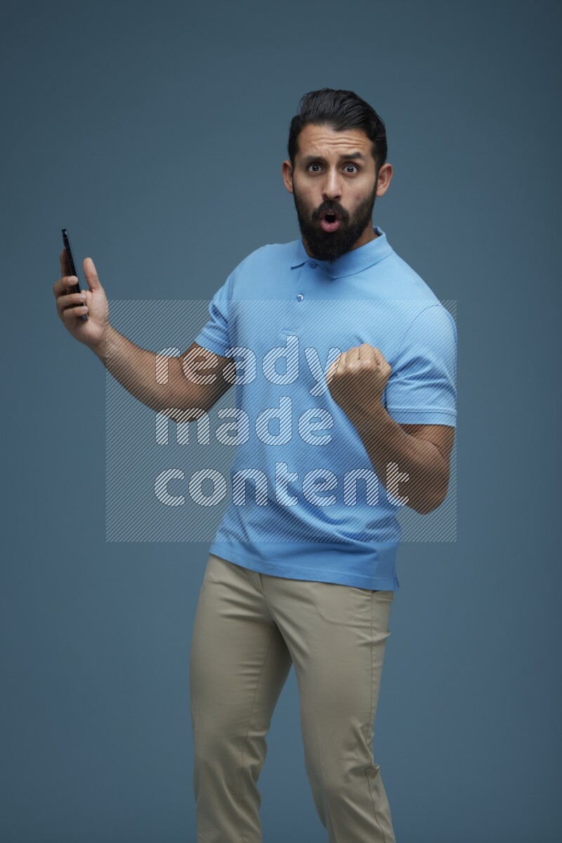 Man posing with a phone in a blue background wearing a Blue shirt