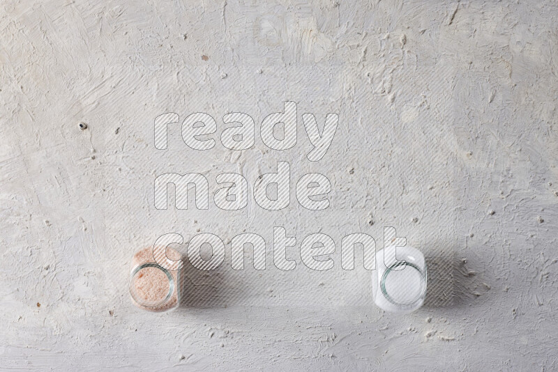 2 وعاء زجاجي احدهمها ممتلئ بملح الهيمالايا الناعم والأخر بملح الطعام على خلفية بيضاء