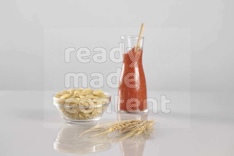Raw pasta with tomatoe pasta with different ingredients such as cherry tomatoes, basil, garlic, bay laurel, cardamom, white pepper, black pepper, red chilis and wheat stalks on light grey background