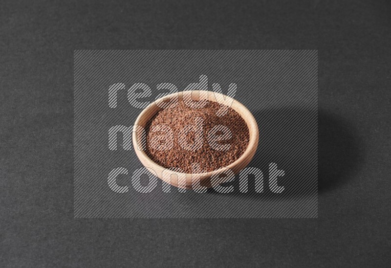 A wooden bowl full of garden cress seeds on a black flooring