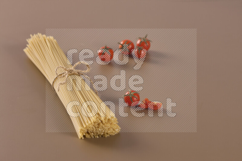 Raw pasta with different ingredients such as cherry tomatoes, garlic, onions, red chilis, black pepper, white pepper, bay laurel leaves, rosemary and cardamom on beige background