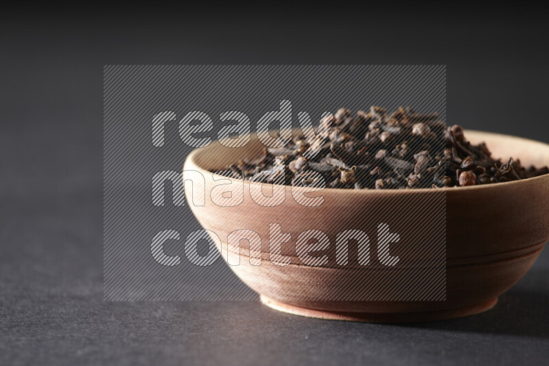 A wooden bowl full of cloves on a black flooring