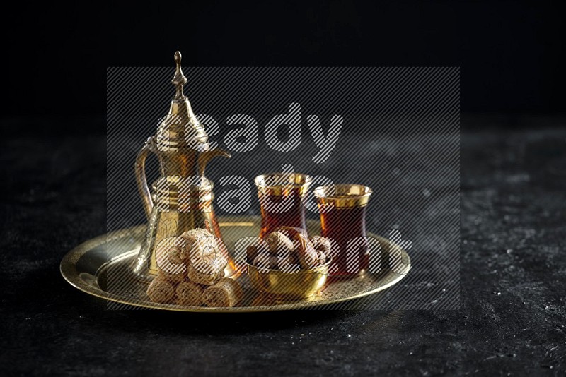 Oriental sweets with dates and a drink on a metal tray in a dark setup