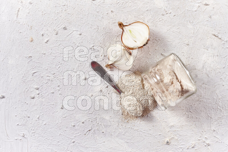 A glass jar full of onion powder flipped with some spilling powder on white background