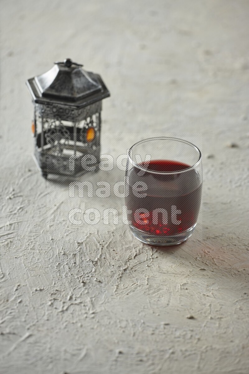 A silver lantern with different drinks, dates, nuts, prayer beads and quran on textured white background