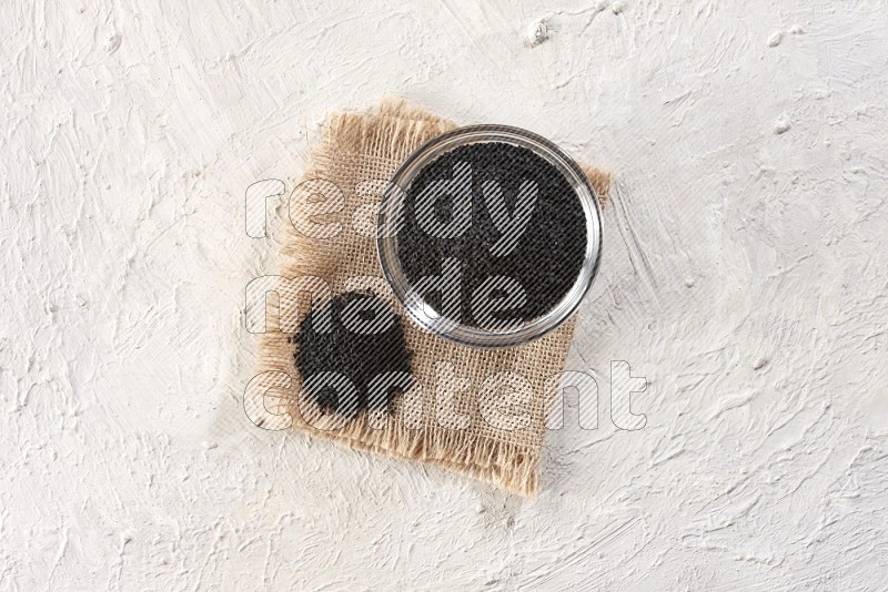 A glass bowl full of black seeds set on a burlap piece on textured white flooring in different angles