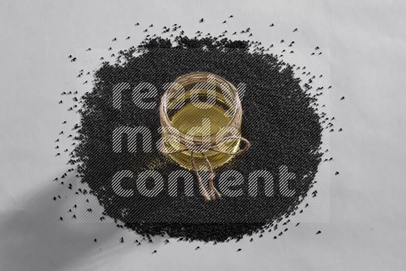 A glass jar full of black seeds oil surrounded by the seeds on a white flooring in different angles