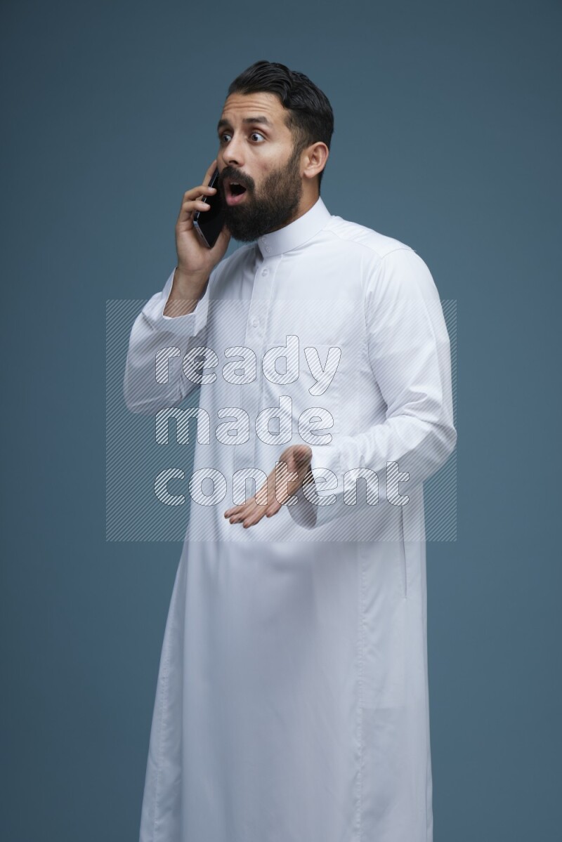 A man having a call on a blue background wearing Saudi Thob