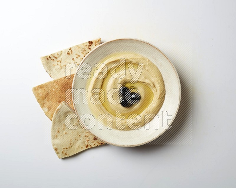 Hummus in a pottry plate garnished with black olives on a white background