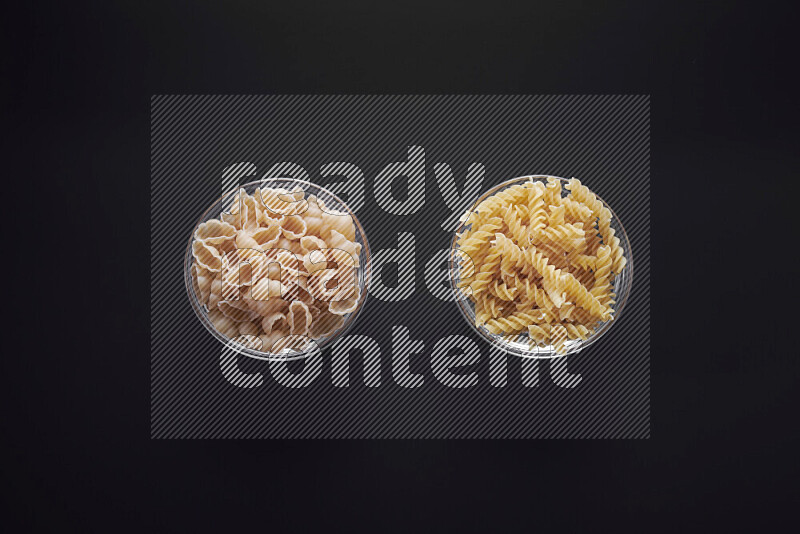 Different pasta types in glass bowls on black background