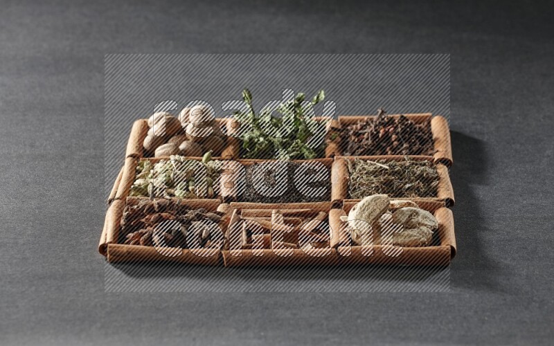 9 مربعات من أعواد القرفة ممتلئة بالشاي في المنتصف محاطة بجوزة الطيب والنعناع المجفف والقرنفل والريحان المجفف والزنجبيل المجفف والقرفة واليانسون والهيل على أرضية سوداء