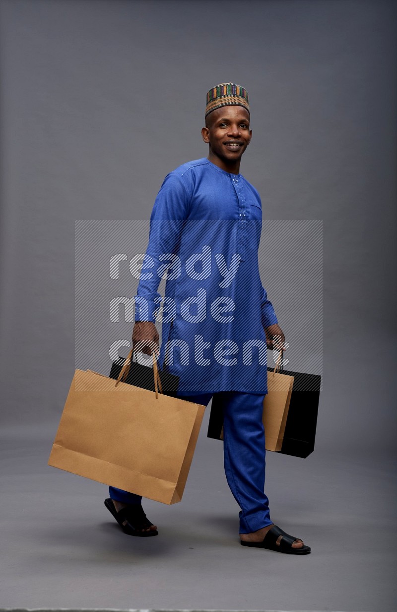 Man wearing Nigerian outfit standing holding shopping bag on gray background