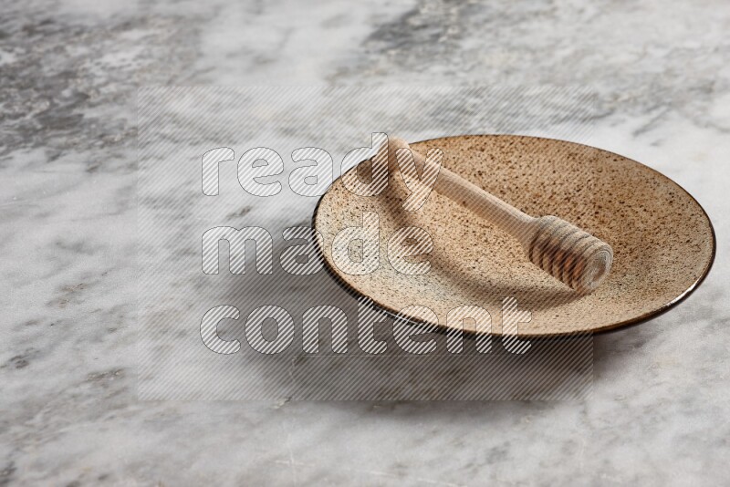 Multicolored pottery plate with wooden honey dipper in it on grey marble background