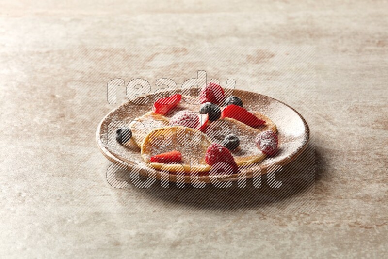 Five stacked mixed berries mini pancakes in a brown plate on beige background
